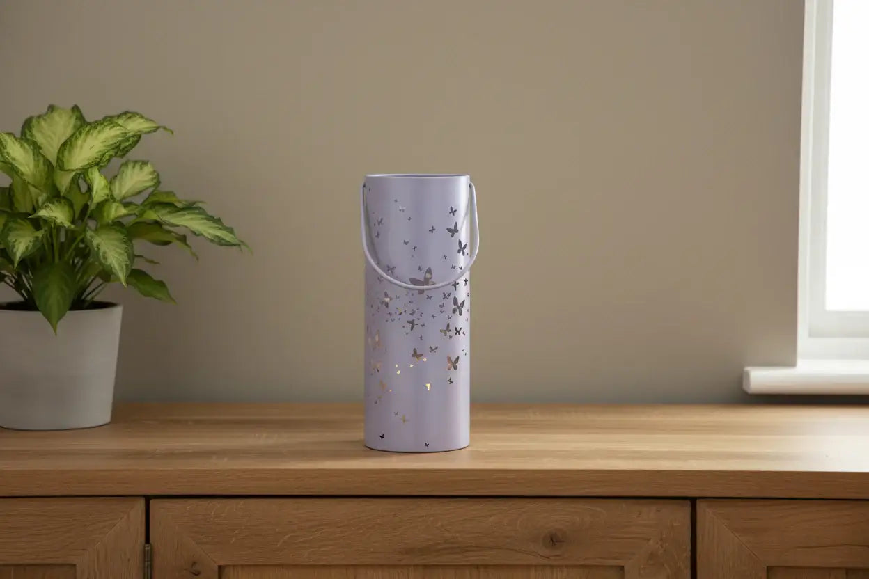 Purple decorative vase with butterfly design on a wooden surface next to a plant