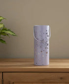 Purple decorative vase with butterfly patterns on a wooden surface next to a plant.