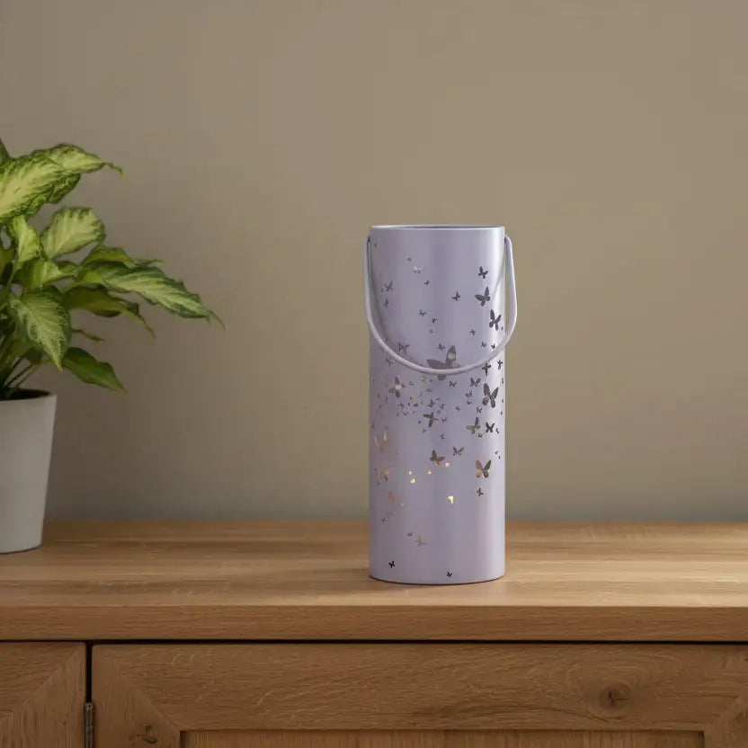 Purple decorative vase with butterfly patterns on a wooden surface next to a plant.