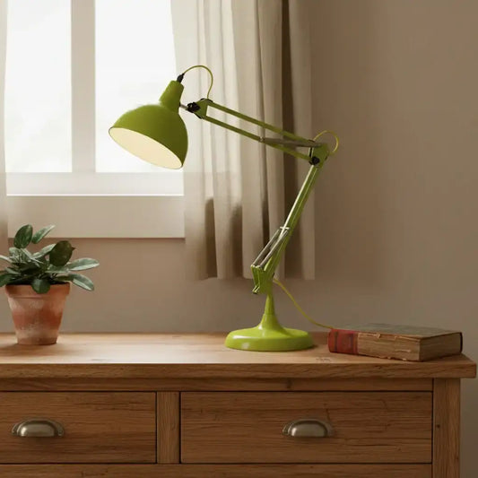 Green desk lamp on a wooden surface with a plant and book in the background