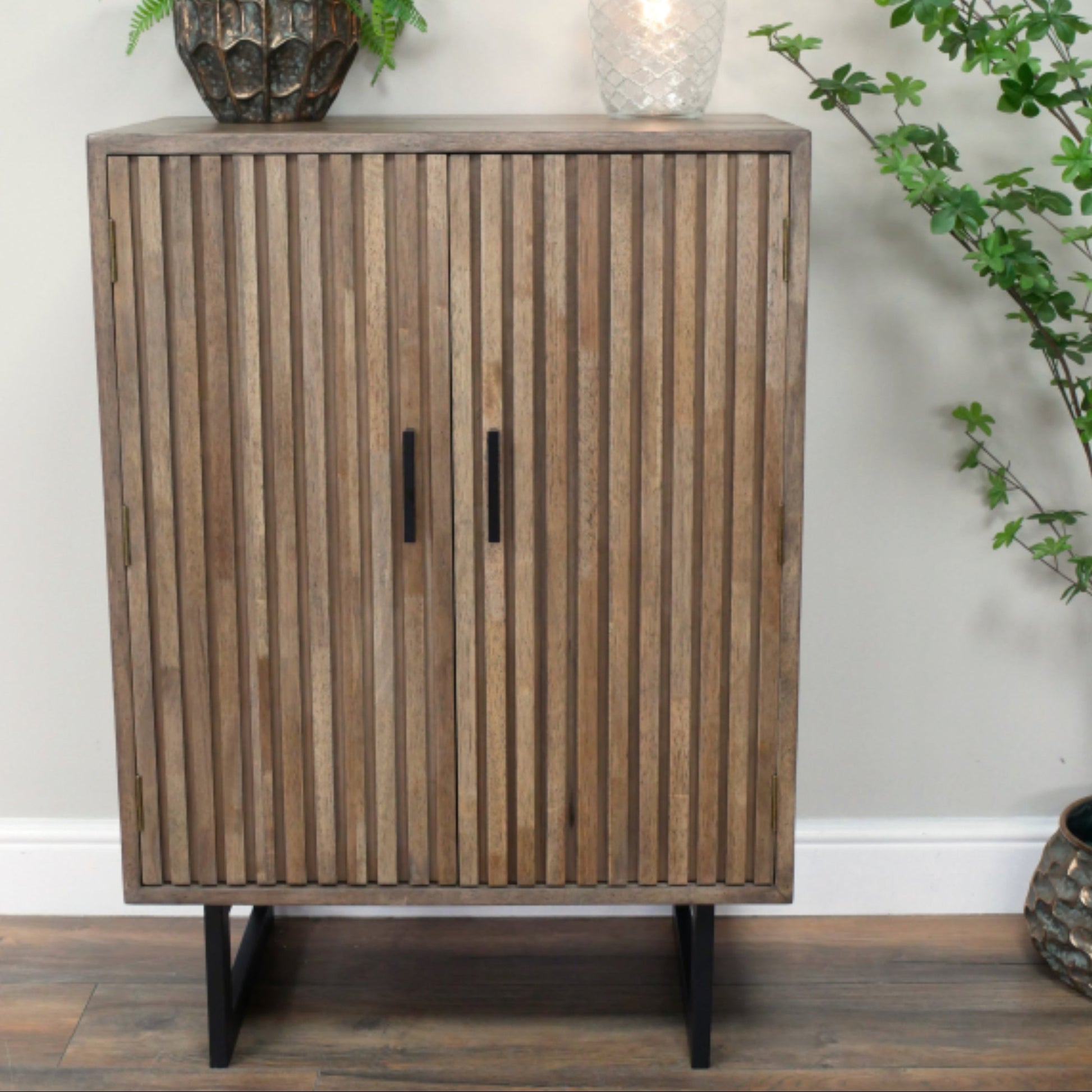 Wooden cabinet with slatted design on a wooden floor with decorative plants.