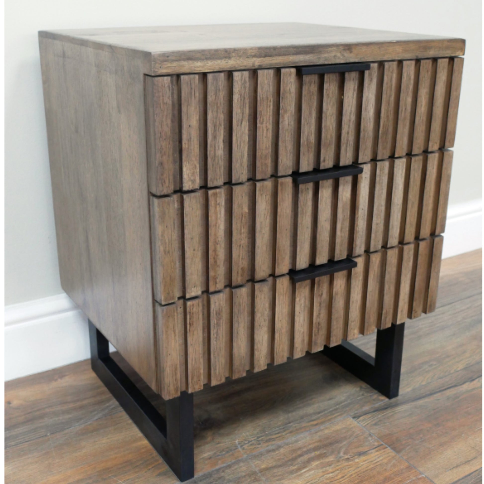 Wooden side table with three drawers on a wooden floor.
