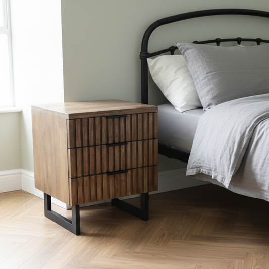 Wooden nightstand next to a bed with gray bedding in a bedroom setting.