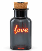 A dark gray glass bottle with a cork stopper, featuring an illuminated orange-red neon-style 'love' sign inside, shown on a plain white background.