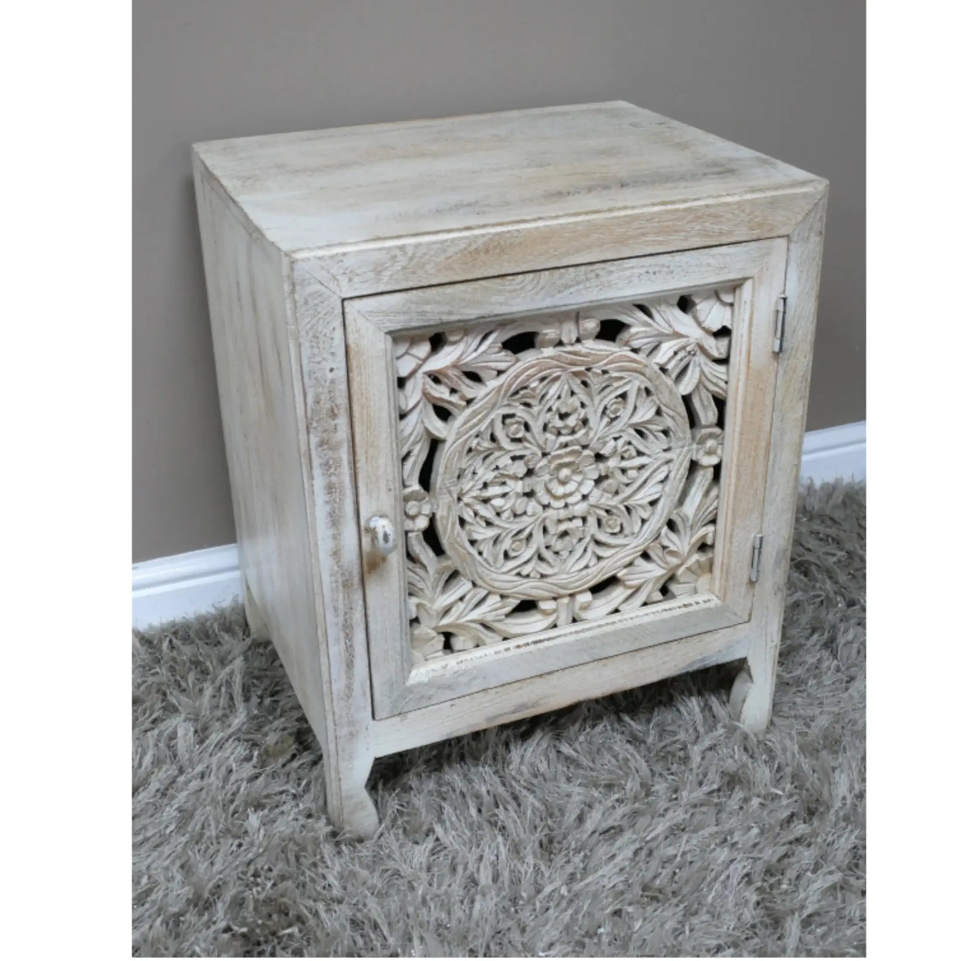Wooden side table with intricate carvings on a gray carpet