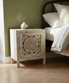 Wooden nightstand with decorative design next to a bed in a bedroom.