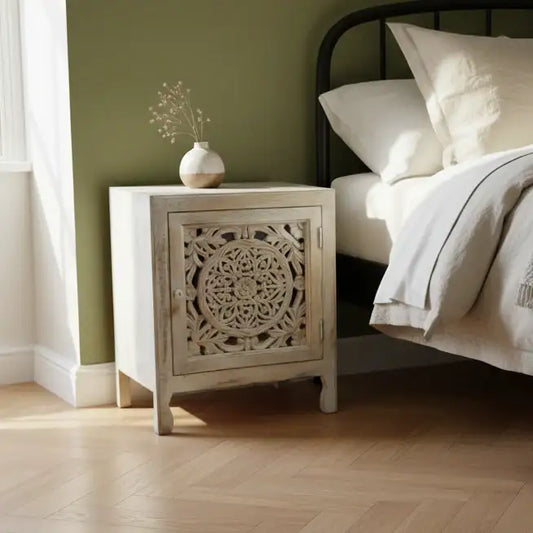 Wooden nightstand with decorative design next to a bed in a bedroom.