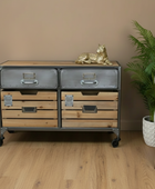 Wooden dresser with metal drawers in a room with a plant and chair.