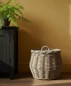 Wicker basket on a wooden floor against a yellow wall with a black cabinet and plant.