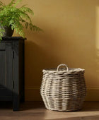 Wicker basket with a lid on a wooden floor against a yellow wall.