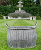 Decorative metal planter on grass with a fountain in the background