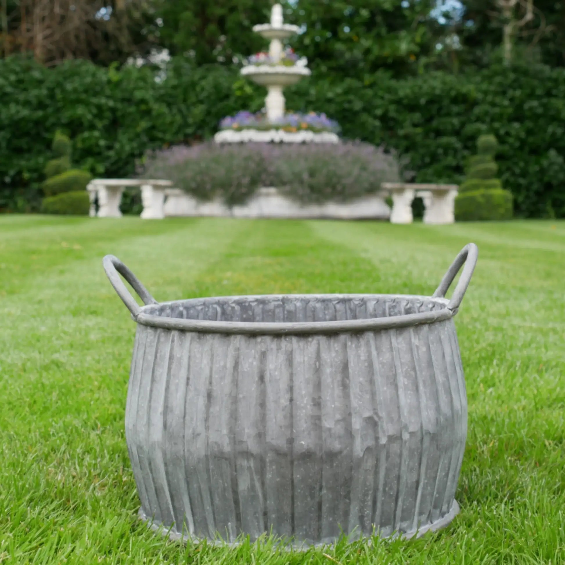 Decorative metal planter on grass with a fountain in the background