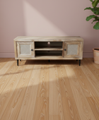 Wooden TV stand with wicker doors on a wooden floor with a plant in the background