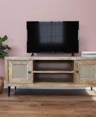 Wooden TV stand with rattan doors on a wooden floor against a gray wall.