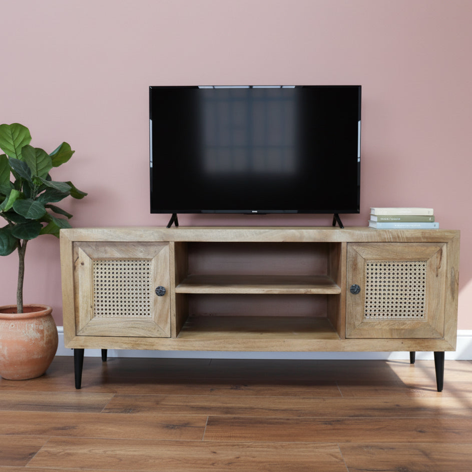 Wooden TV stand with rattan doors on a wooden floor against a gray wall.