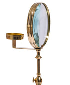 A brass magnifying mirror with an adjustable stand and a small brass cup holder on the side, shown against a plain white background.