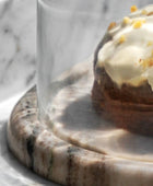 Pastry with white icing and yellow sprinkles under a glass dome on a marble surface