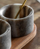 Two stone cups on a wooden surface with a spoon inside one of them.
