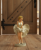 Statue of a woman in a white dress on a wooden floor with a wooden door in the background