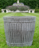 Decorative metal planter on grass with garden in the background