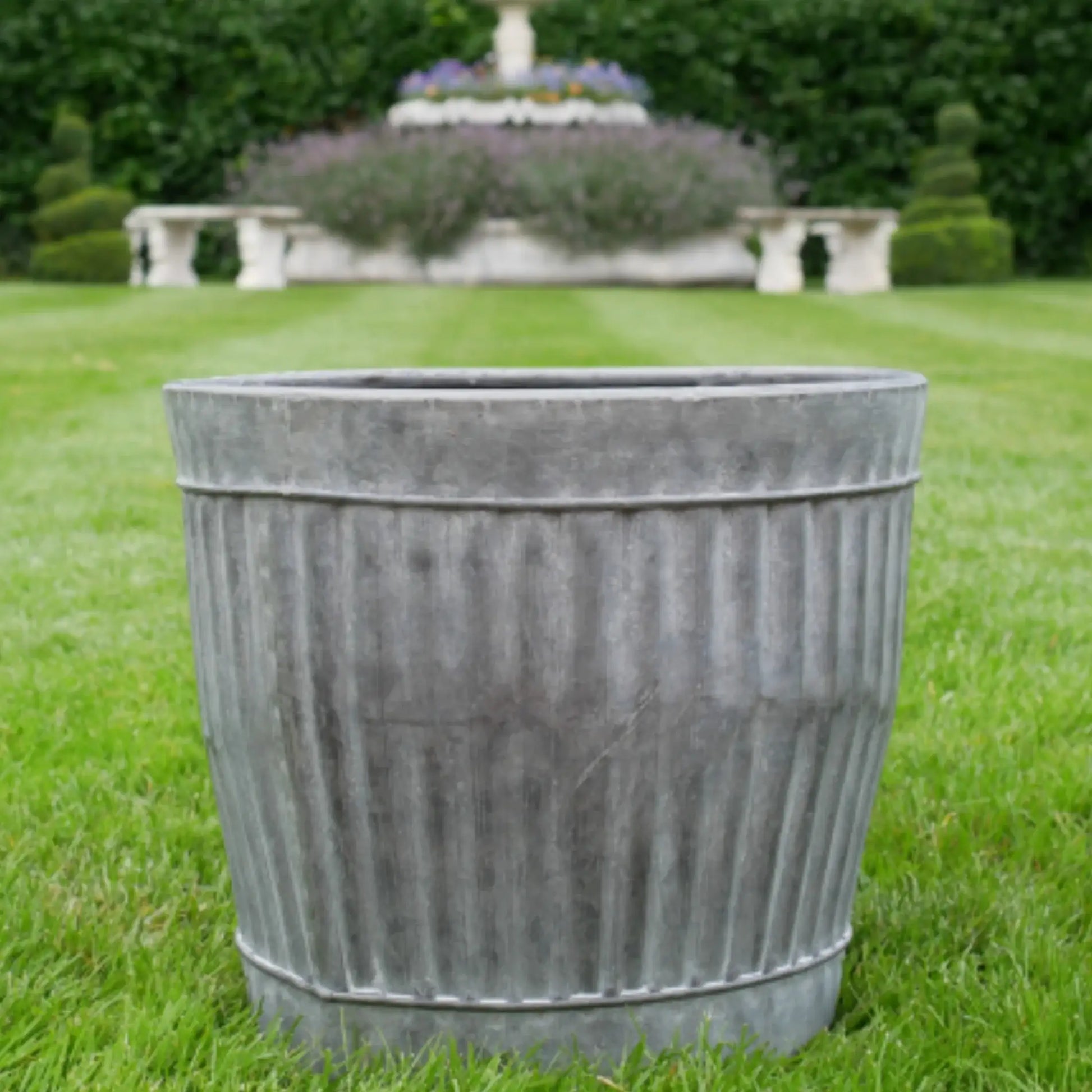 Decorative metal planter on grass with garden in the background