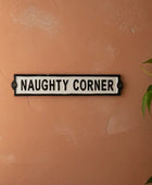 Decorative sign on a wall with 'NAUGHTY CORNER' text, next to a potted plant.