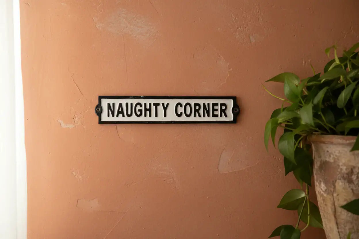 Decorative sign on a wall with 'NAUGHTY CORNER' text, next to a potted plant.