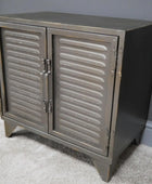 Metallic cabinet with shutter doors on a gray carpeted floor against a gray wall.