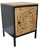 Small cabinet with wooden top and intricate carvings on a black frame against a white wall.