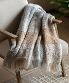 Textured blanket draped over a wooden chair with a plant in the background