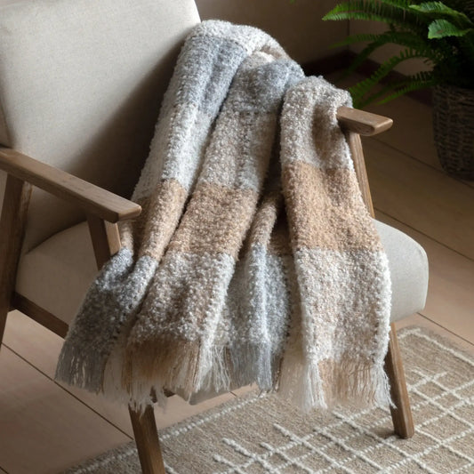 Textured blanket draped over a wooden chair with a plant in the background