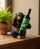A novelty figurine of a seated chimpanzee holding a wine bottle, placed on a wooden windowsill next to a potted fern.
