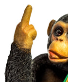 A close-up of a chimpanzee figurine or toy against a plain white background, with the animal's face and raised hand visible and part of a green object in the lower right corner.