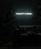 Neon sign reading 'NAUGHTY CORNER' in a dimly lit room with a couch and plant.