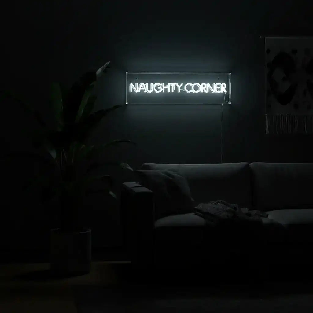 Neon sign reading 'NAUGHTY CORNER' in a dimly lit room with a couch and plant.