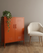Orange cabinet with a plant next to a beige chair in a room with a wooden floor and gray walls.