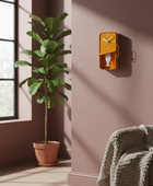 Yellow wall clock on a pink wall with a plant and chair in the foreground