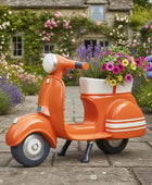 Orange scooter-shaped planter with flowers in a garden setting