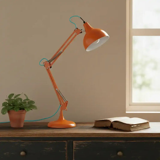 Orange desk lamp on a wooden surface with a plant and book in a room with a window.