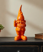 Orange gnome figurine on a wooden surface with a plant and book in the background