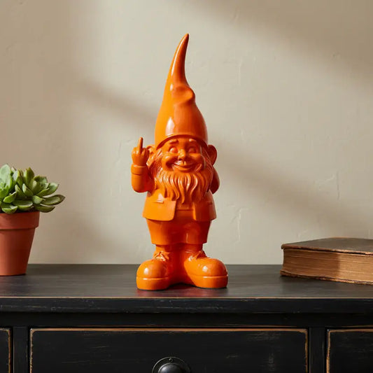Orange gnome figurine on a wooden surface with a plant and book in the background