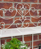 Decorative white metal bench with intricate designs against a brick wall.
