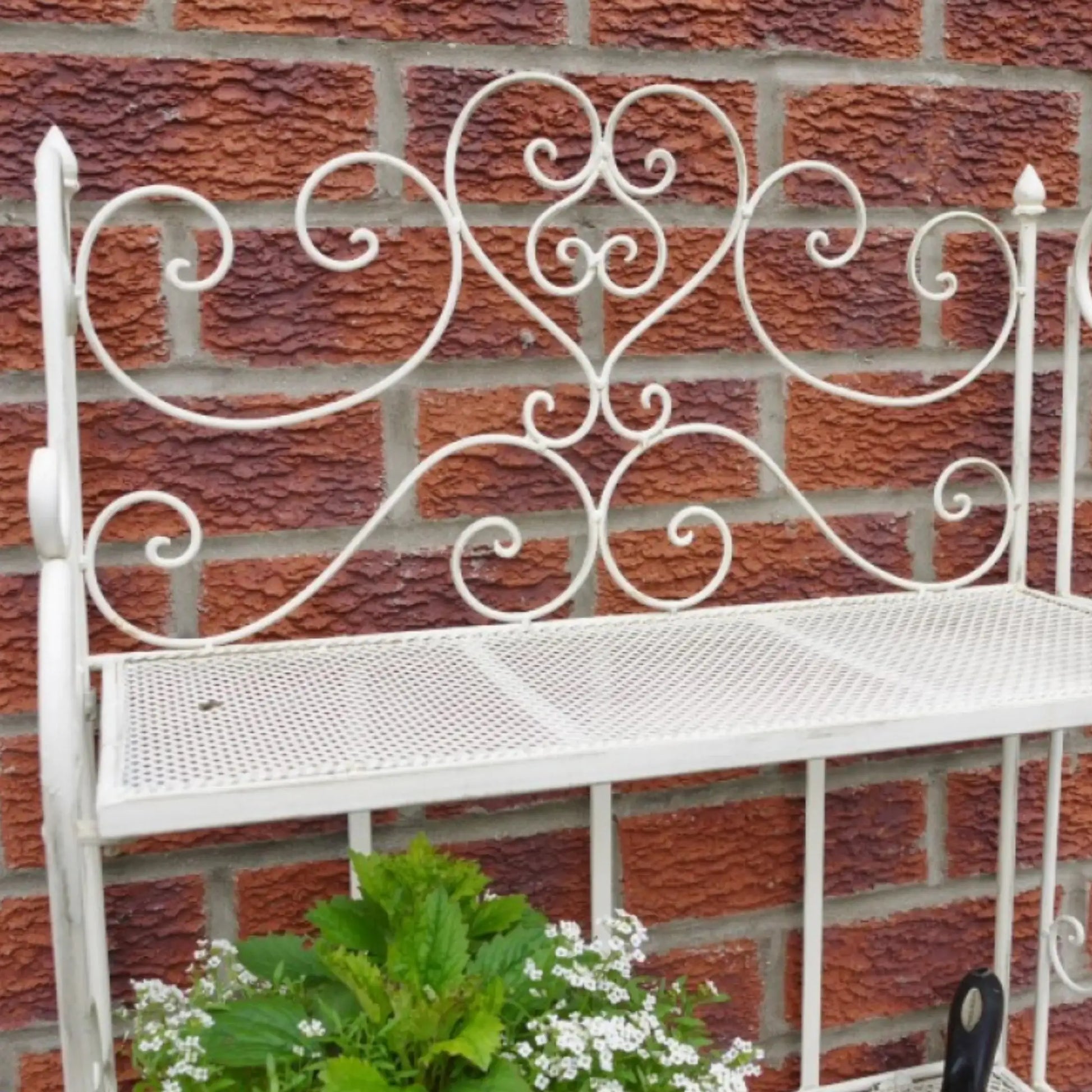 Decorative white metal bench with intricate designs against a brick wall.