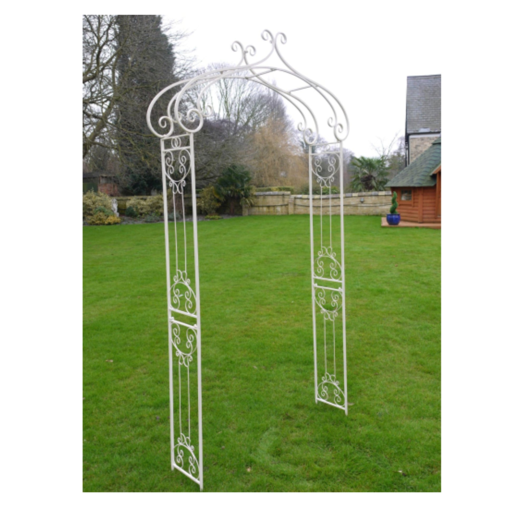 Decorative white metal garden archway on a grassy lawn with trees and a building in the background.