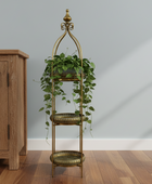 Decorative gold plant stand with green plants against a light gray wall.