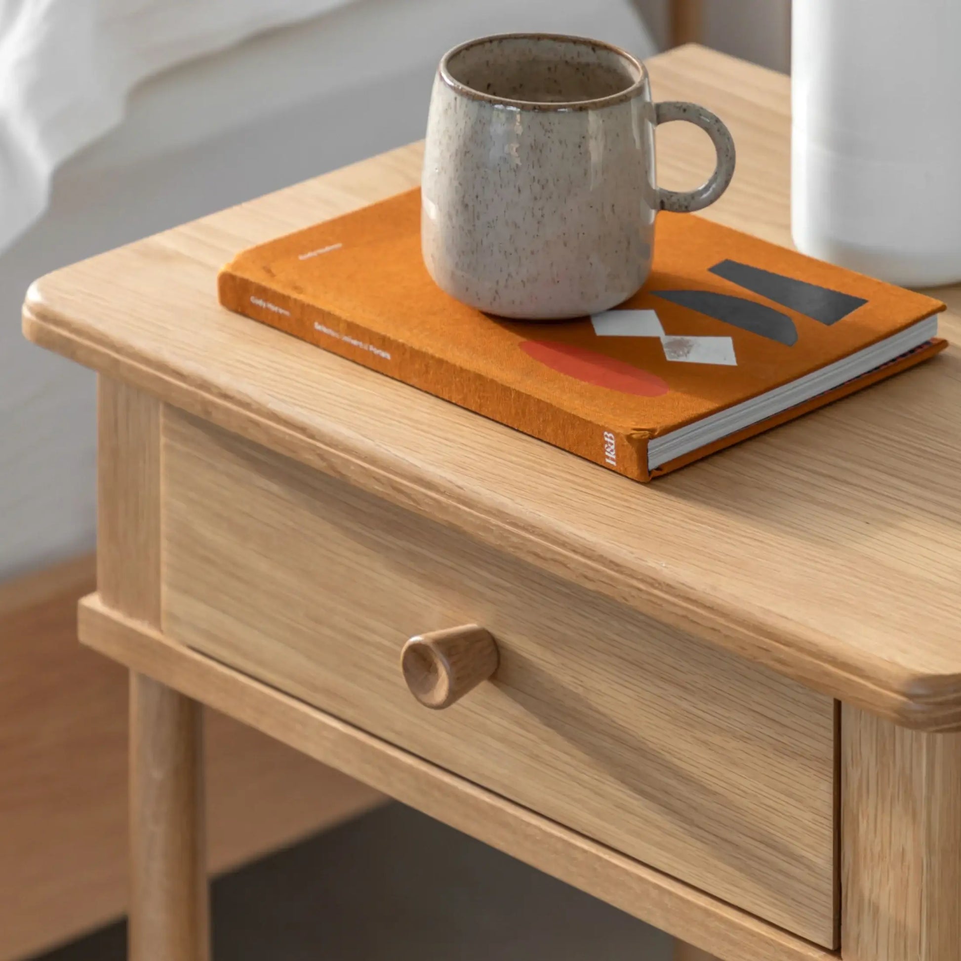 Wooden side table with an orange book and ceramic mug on top
