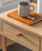 Wooden side table with an orange book and ceramic mug on top