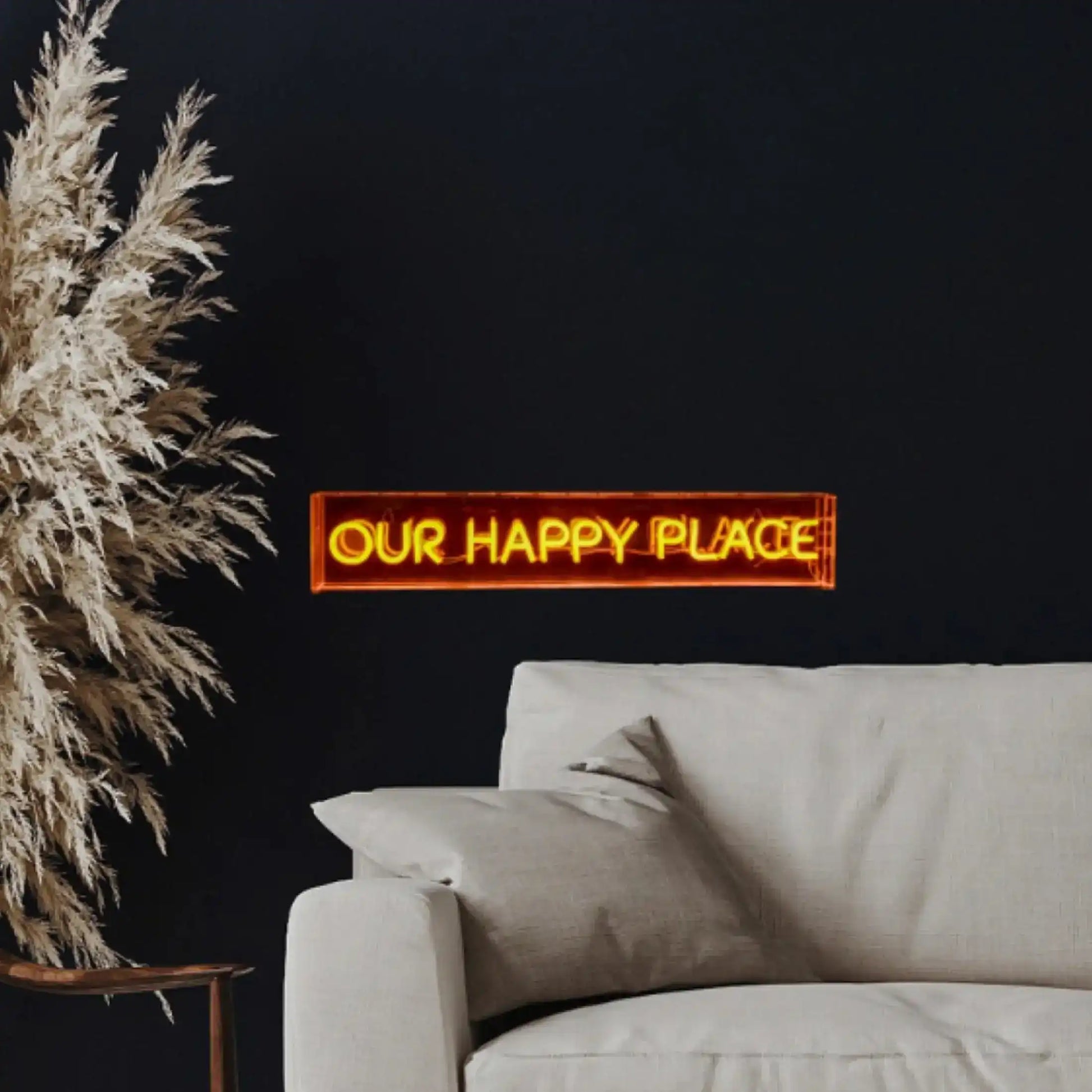 Neon sign reading 'Our Happy Place' above a sofa with decorative pampas grass.