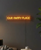 Neon sign reading 'OUR HAPPY PLACE' on a dark wall with a plant and couch in the background.