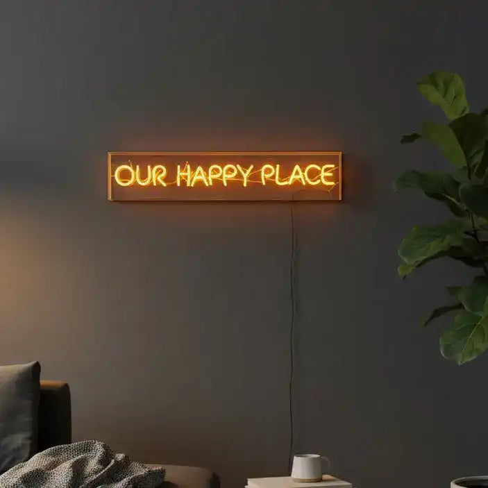 Neon sign reading 'OUR HAPPY PLACE' on a dark wall with a plant and couch in the background.